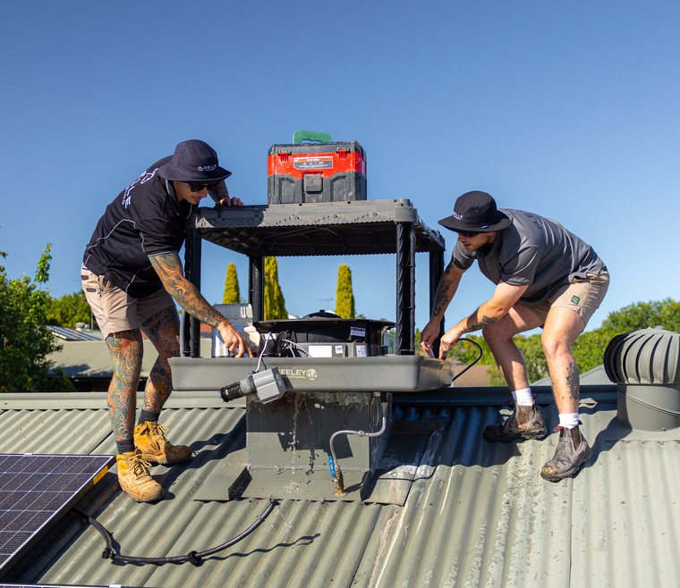 Two technicians working on a rooftop evaporative cooler